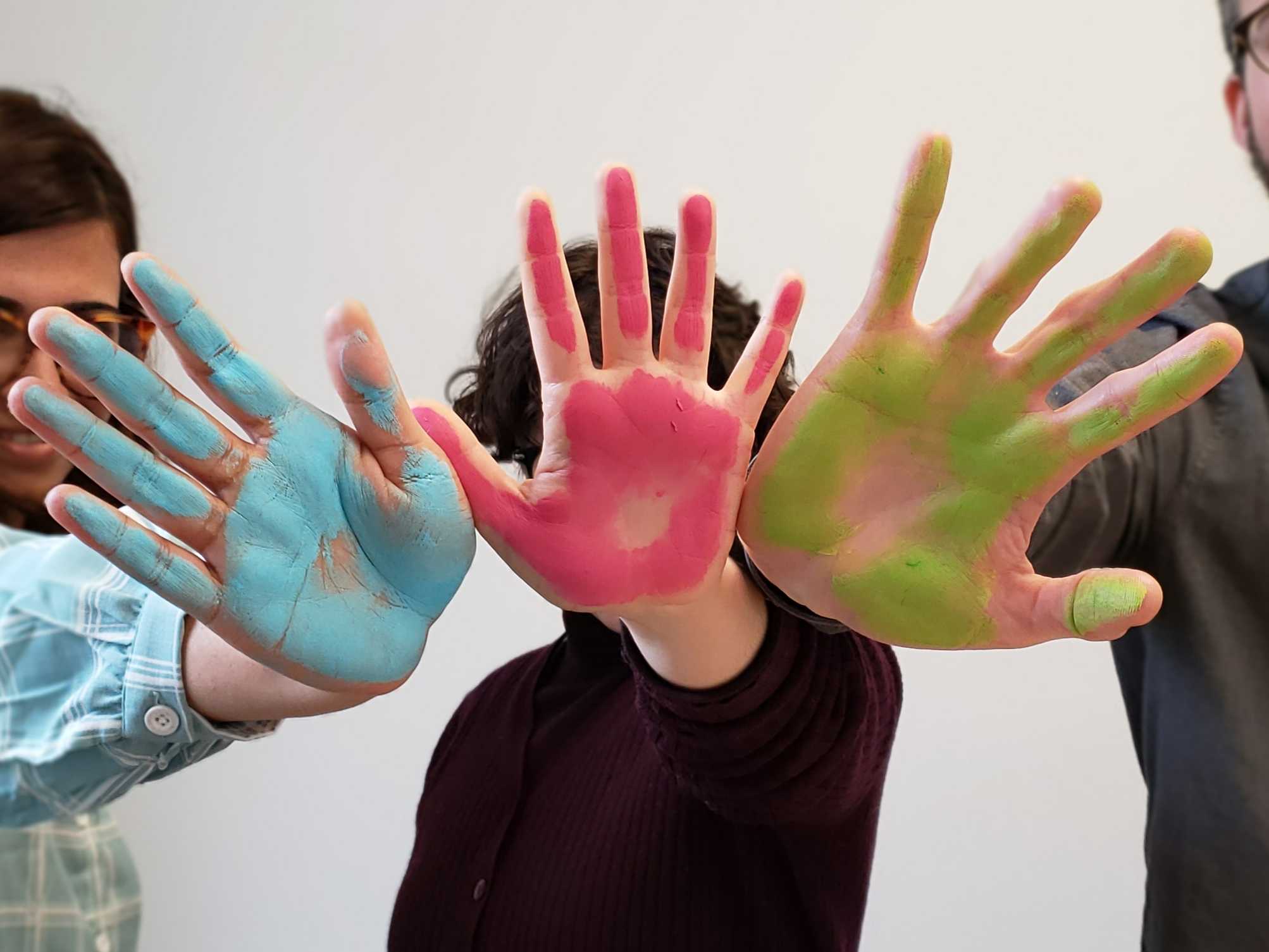Three PhenoTips team members hold their blue, pink, and green painted hands up to the camera to create the image of the Rare Disease Day logo. Taken on Rare Disease Day 2020.